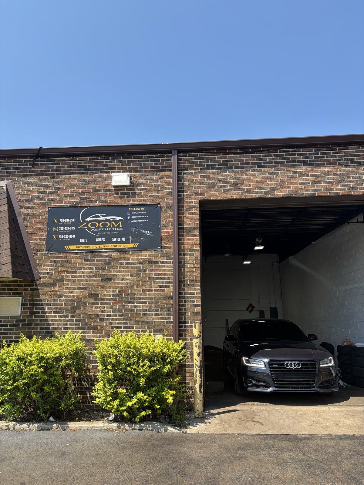 Zoom Aesthetics storefront in Orland Park — brick shop with the Zoom Aesthetics banner above the open bay and an Audi inside